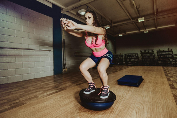 Sportliche Frau hockt auf dem Bosu-Ball im Fitnessstudio