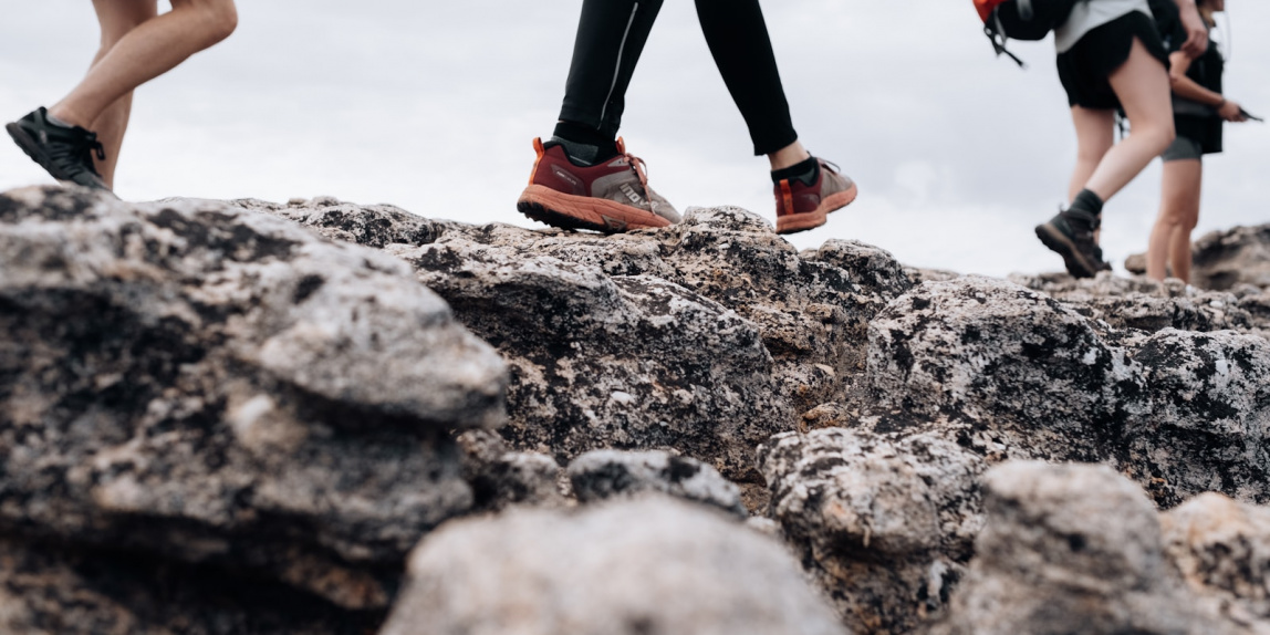 person in black pants and orange and black nike sneakers standing on rocky ground during daytime