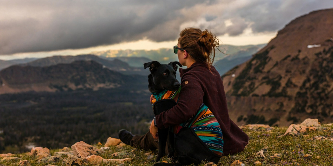 woman sitting beside black dog on mountain