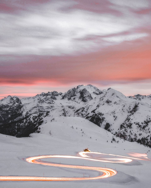 A winding road glowing under sunset skies amidst the snowy peaks of the Veneto Alps.