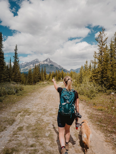 woman in blue t-shirt and black shorts standing on dirt road near green trees during