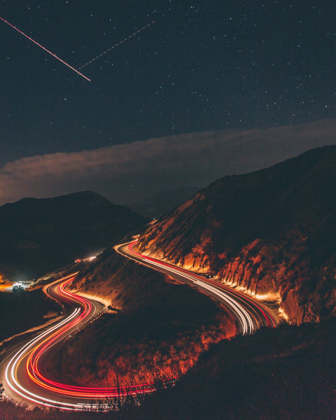A captivating long exposure shot of a winding highway at night with car light trails under a starry sky.