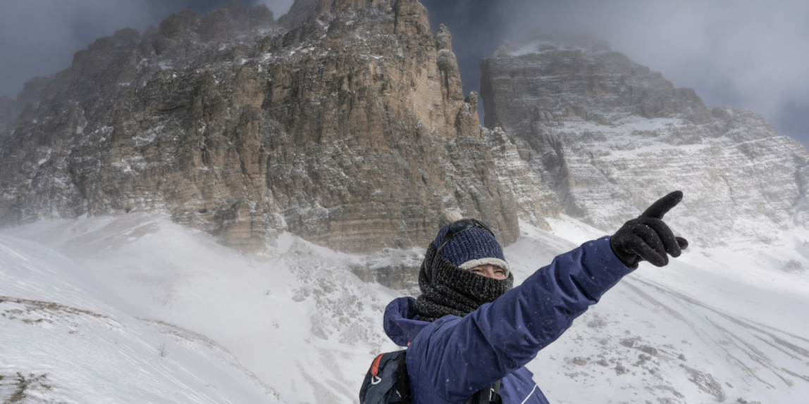 a man in a blue jacket pointing at a mountain