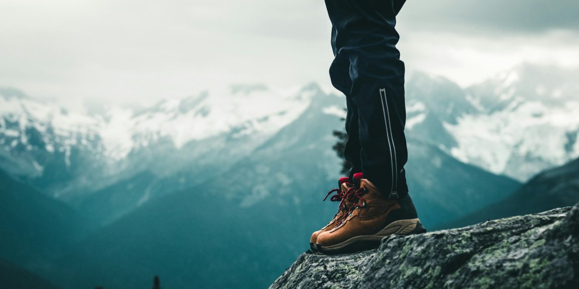 person in black pants and brown leather shoes standing on rock